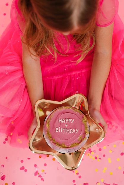 Menina de vestido rosa segura um delicioso bolo bento doce com a inscrição feliz aniversário