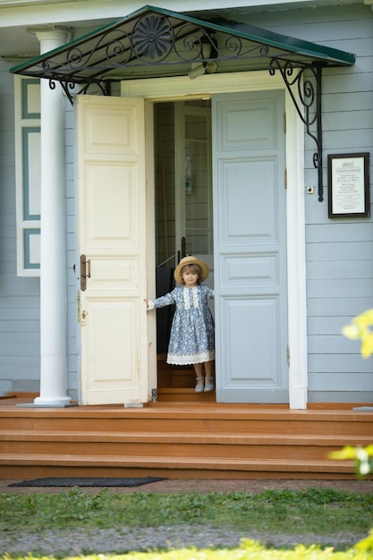 Menina de vestido vintage e chapéu de palha abre a porta para a casa da aldeia