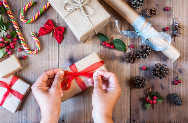 Menina decora o presente de Natal, amarra o laço vermelho.