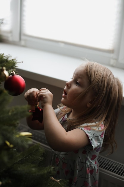 Menina decorando a árvore de natal com brinquedos e enfeites Garoto bonito se preparando para casa para a celebração de natal