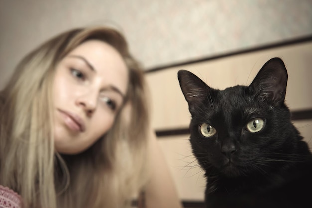 Foto menina deitada na cama com seu gato mal é um gato duro preto machucou o gato o gato foi ofendido por sua amante ressentimento tristeza e frustração no rosto do animal