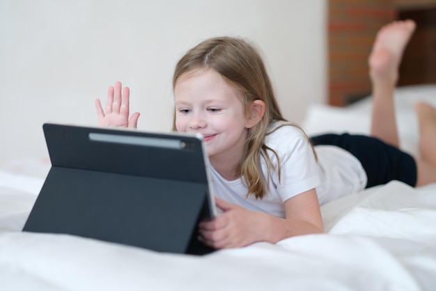 Menina deitada na cama e acenando com a mão na tela do tablet