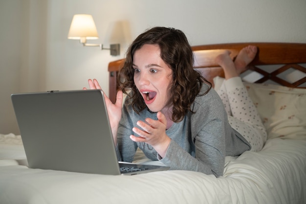 Foto menina deitada na cama em seu quarto usando o computador surpresa mulher em uma videochamada em um laptop