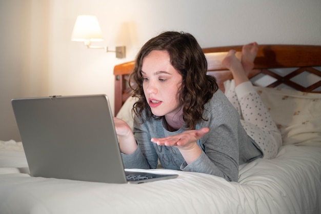 Foto menina deitada na cama em seu quarto usando o computador surpresa mulher em uma videochamada em um laptop