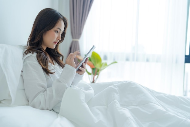 Menina deitada na cama jogando computador tablet no quarto