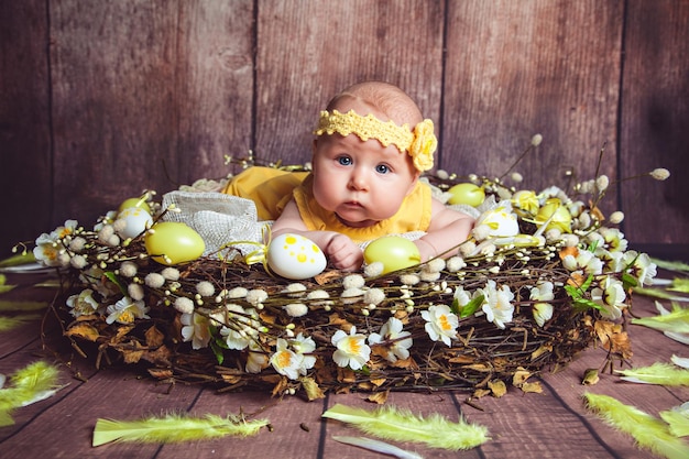 Menina deitada no ninho gigante decorado com ovos de páscoa e penas