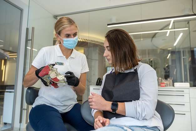 Menina dentista mostra um modelo de mandíbula como um auxílio visual para uma paciente menina Uma amostra de mandíbulas para treinamento de dentistas ensina como cuidar dos dentes Saúde dental Dentista feminina