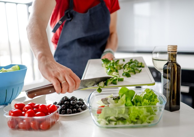 Menina derrama pepinos picados em uma tigela para salada grega em casa em uma cozinha brilhante