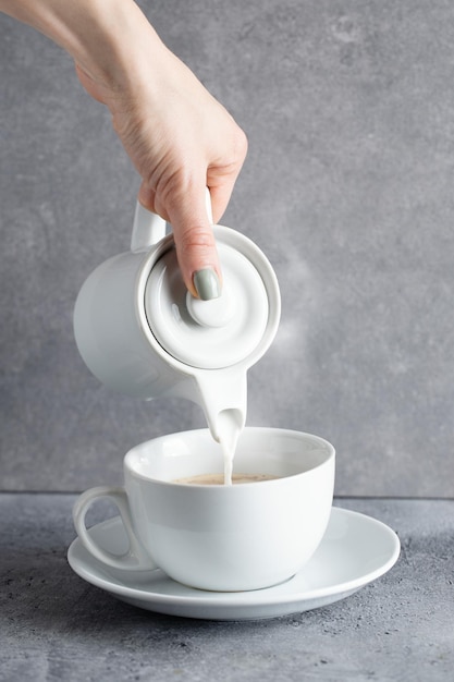 Menina derramando leite do jarro na xícara de café