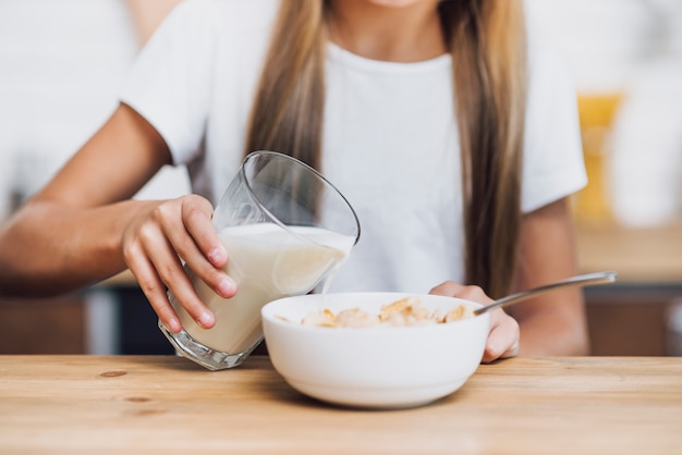 Foto menina derramando leite em uma tigela de cereais