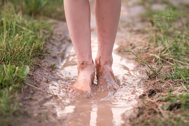 Menina descalça atravessa poças d'água após a chuva de verão na zona rural.