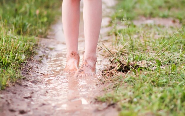 Menina descalça atravessa poças d'água após a chuva de verão na zona rural.