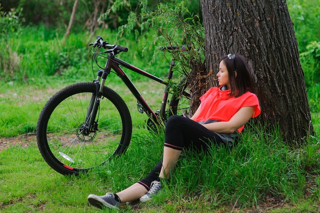 Menina descansando depois de andar de bicicleta perto de uma árvore