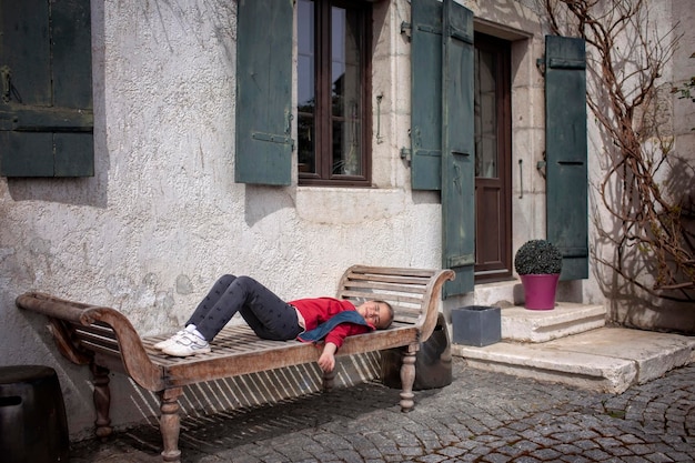 Menina descansando em um banco ao lado de uma casa rústica com persianas verdes