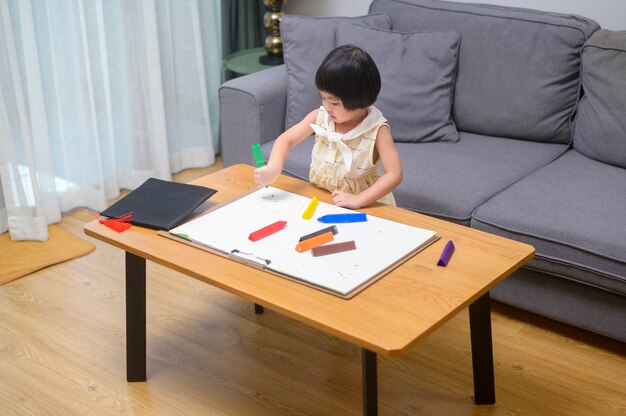 Menina desenhando com lápis de cor na sala de estar em casa.