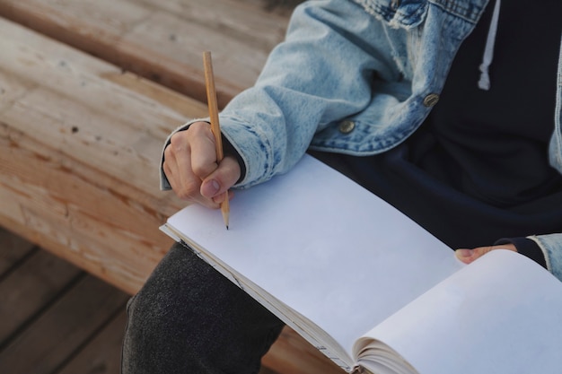 Menina desenhando com um lápis em uma página em branco do caderno de desenho