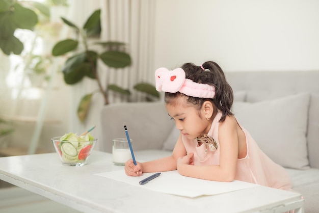 Menina desenhando na mesa com ferramentas de pintura dentro de casa