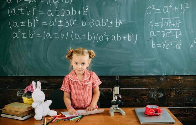 Menina desenhando no fundo do quadro-negro Menina na mesa do professor na aula de escola Uma escola com infusão de arte