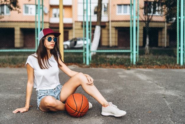 Menina desportiva consideravelmente nova com a bola do basquetebol ao ar livre.