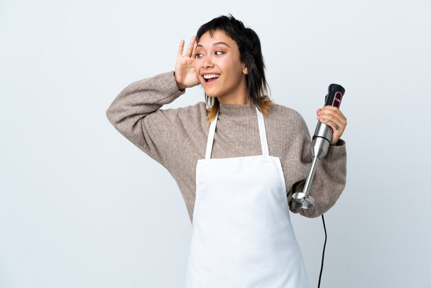 Menina do chef usando o liquidificador de mão sobre branco isolado, ouvindo algo