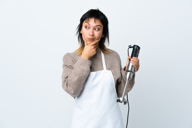 Menina do chef usando o liquidificador de mão sobre branco isolado, pensando uma idéia