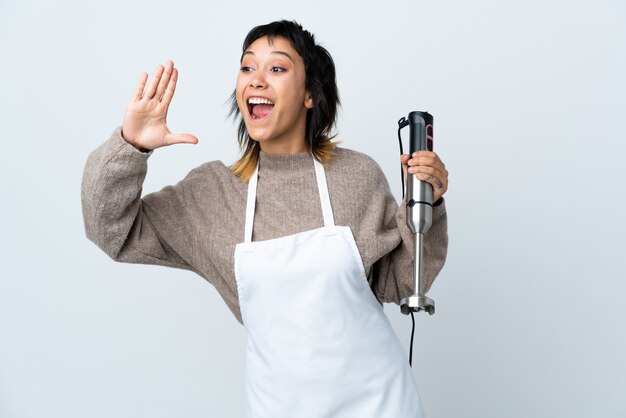 Menina do chef usando o liquidificador de mão sobre isolado branco gritando com a boca aberta