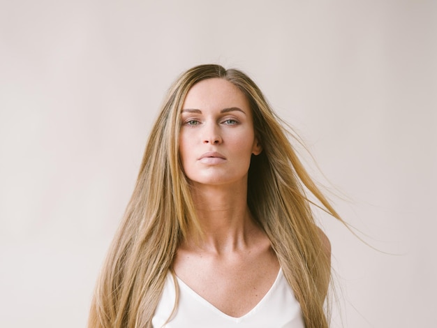 Menina do retrato natural de mulher bonita com longos cabelos loiros sobre uma parede cinza branca. Tiro do estúdio.