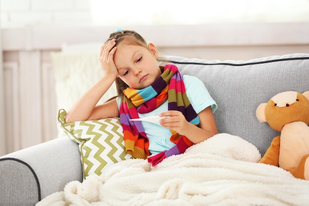 Menina doente com frio sentado no sofá