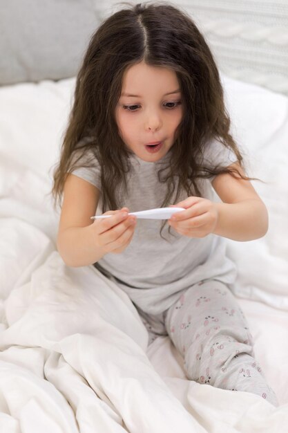 Menina doente deitada na cama com termômetro