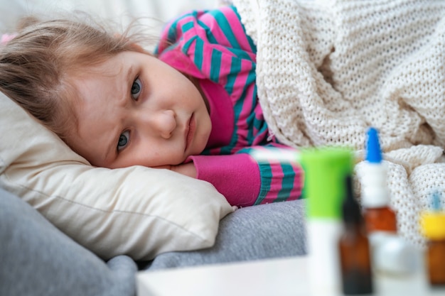 Menina doente está deitado no sofá, embrulhado em um cobertor. na mesa medicamentos.