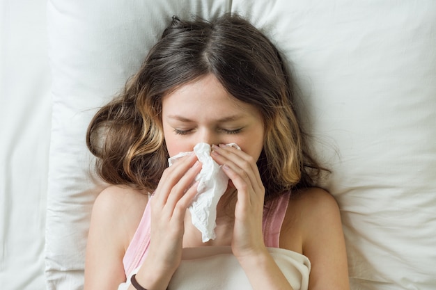 Menina doente na cama espirros no lenço no quarto