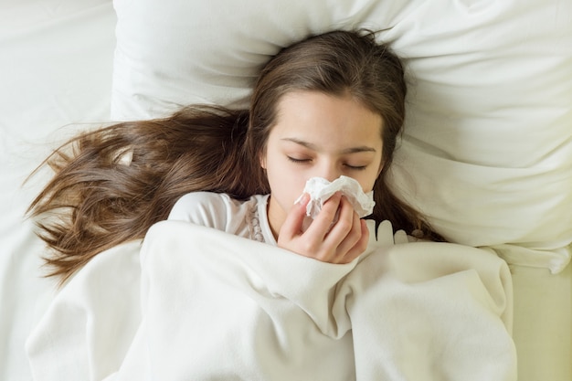 Menina doente na cama espirros no lenço no quarto