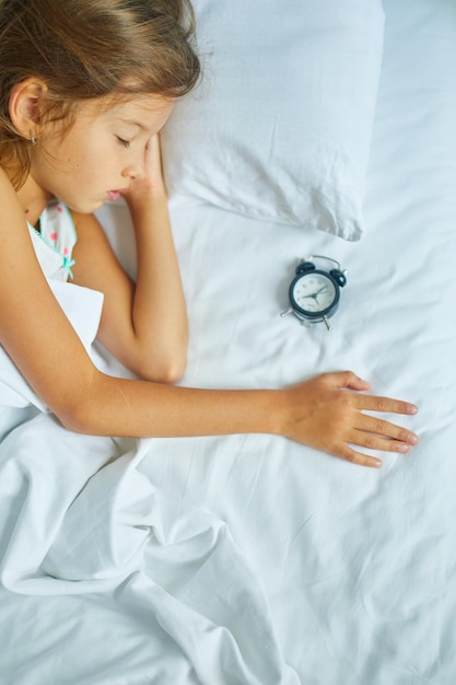 Foto menina dormindo em uma cama grande e aconchegante com roupa de cama branca à tarde em casa
