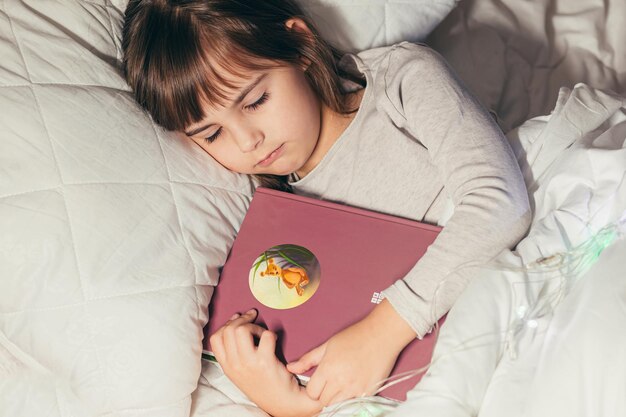 Menina dormindo na cama com um livro nas mãos