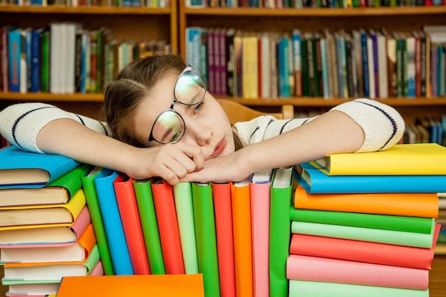 Menina dormindo nos livros da biblioteca