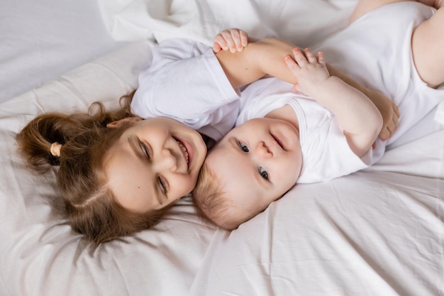 Menina e bebê em roupas brancas estão deitados na cama na roupa de cama branca. irmão e irmã se aquecem na cama. sono e descanso das crianças. hygge, estilo de vida. espaço para texto. Foto de alta qualidade