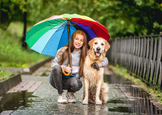 Menina e golden retriever sob o guarda-chuva