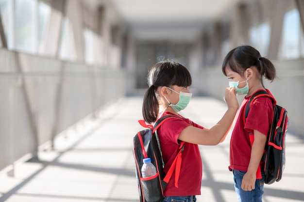 Menina e irmã usando máscara facial, indo para a escola durante o surto de coronavírus. máscara de segurança para prevenção de doenças. mãe e filho na escola durante 19 pandemias.