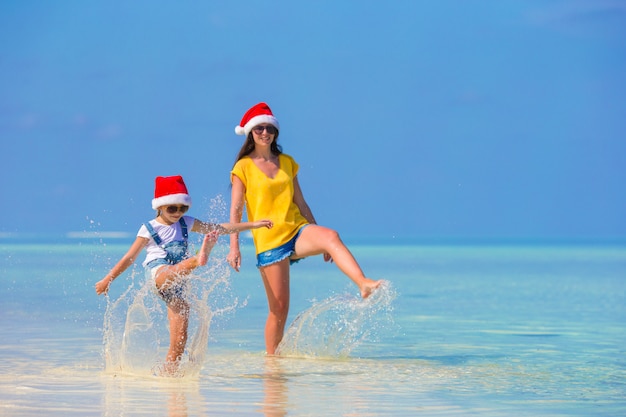 Menina e jovem mãe no chapéu de papai noel durante as férias de praia