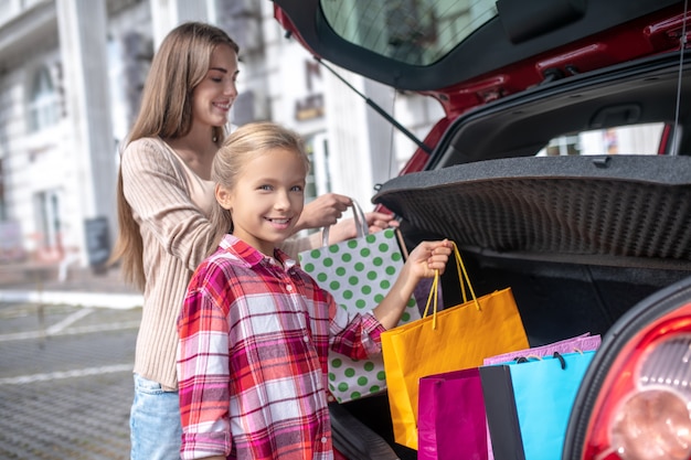 menina e jovem tirando sacolas de compras do porta-malas do carro