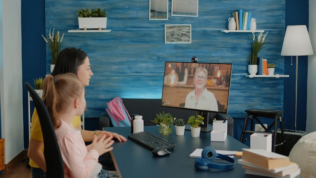 Menina e mãe conversando com a avó na videochamada, criando uma ligação em conferência online com a webcam. criança e pai conversando com a avó no computador para comunicação remota.