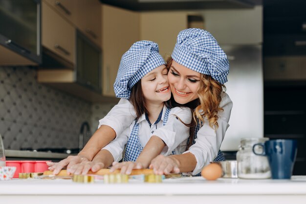 Menina e mãe estenda a massa com um rolo juntos.