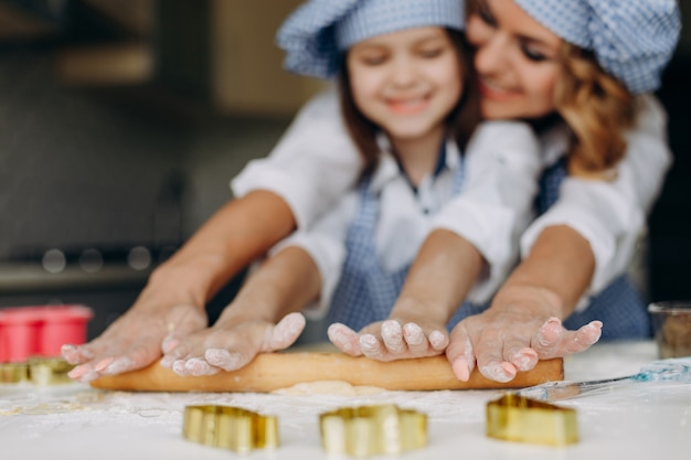 Menina e mãe estenda a massa com um rolo juntos.