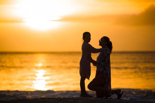 Menina e mãe feliz silhueta por do sol na praia