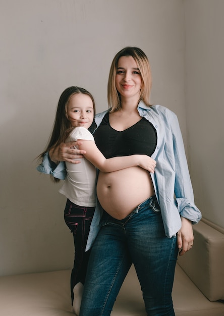 Menina e mãe grávida amando a irmãzinha ao lado da barriga da mãe. família feliz