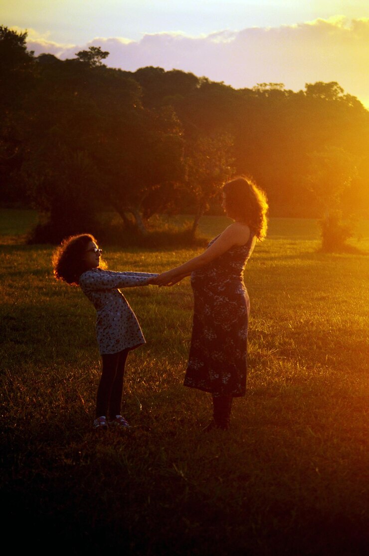 Foto menina e mãe grávida de mãos dadas no campo durante o pôr do sol
