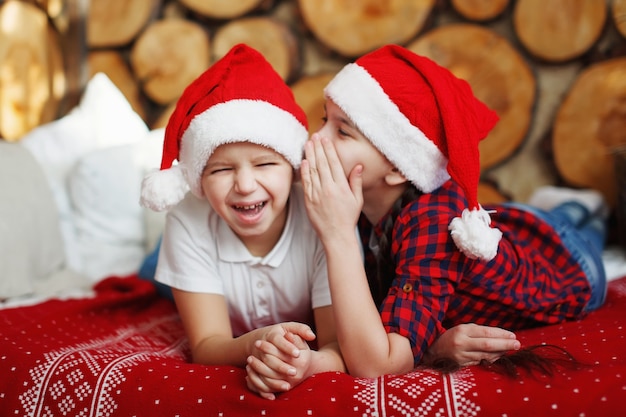 Menina e menino adolescente com um chapéu vermelho de Natal conversando, deitada na cama em um interior festivo