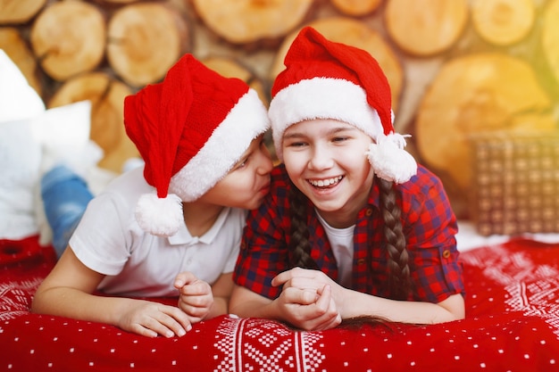 Menina e menino adolescente com um chapéu vermelho de Natal conversando, deitada na cama em um interior festivo