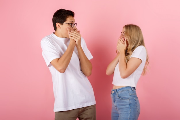 Menina e menino chocados cobrem a boca e se olham