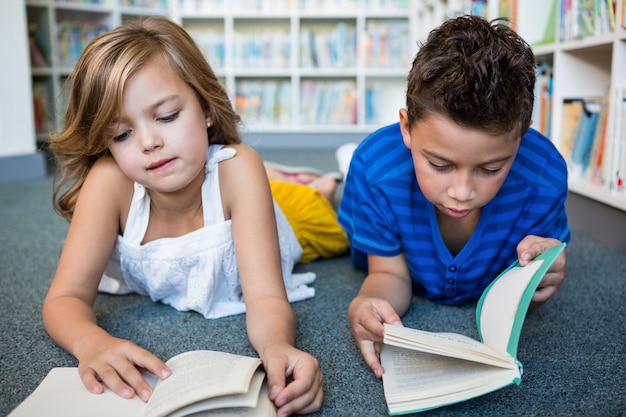 Menina e menino lendo livros na biblioteca da escola